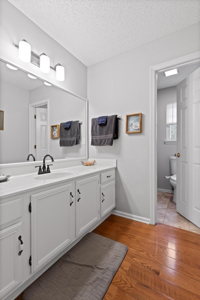 bathroom featuring vanity, wood-type flooring, toilet, and a textured ceiling