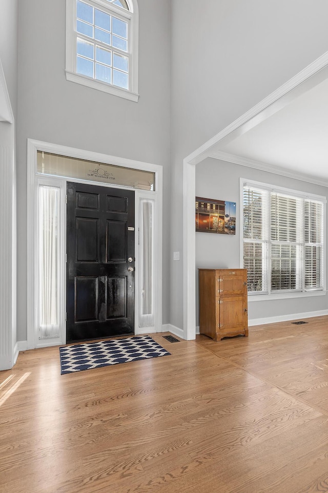 foyer entrance with a towering ceiling, ornamental molding, and hardwood / wood-style floors