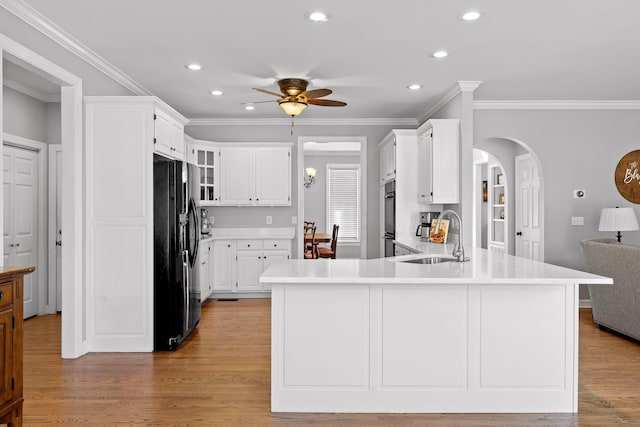 kitchen with sink, ceiling fan, white cabinetry, black fridge, and light wood-type flooring