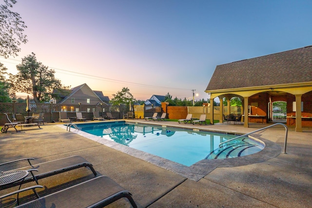 pool at dusk featuring ceiling fan and a patio area