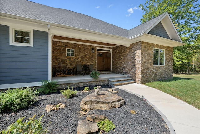 view of exterior entry featuring stone siding, covered porch, and a shingled roof