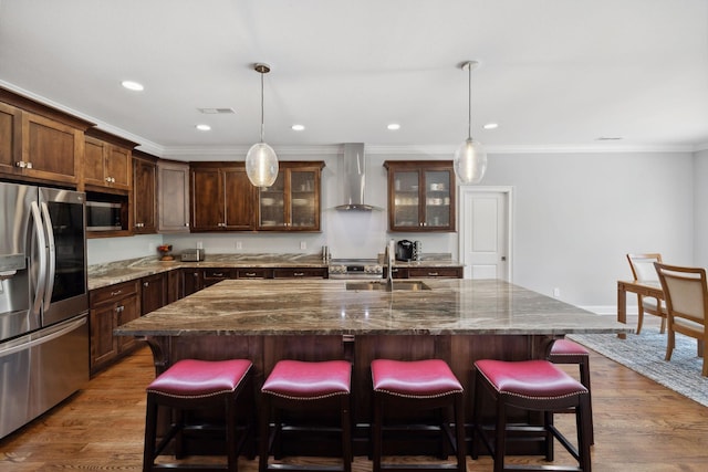 kitchen featuring sink, an island with sink, wall chimney exhaust hood, and appliances with stainless steel finishes