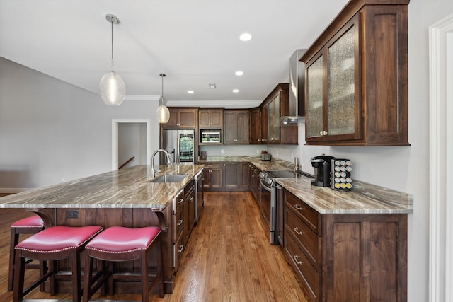 kitchen featuring appliances with stainless steel finishes, a breakfast bar, a large island, light stone countertops, and wall chimney range hood