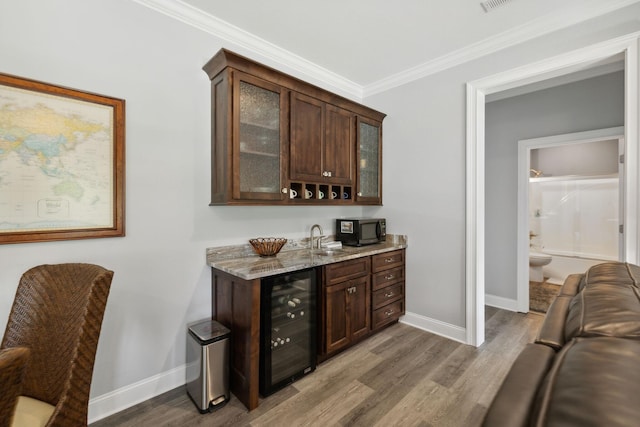 bar with wine cooler, dark brown cabinets, hardwood / wood-style floors, and light stone counters