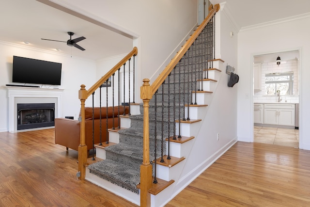 staircase with hardwood / wood-style floors, ceiling fan, sink, and ornamental molding