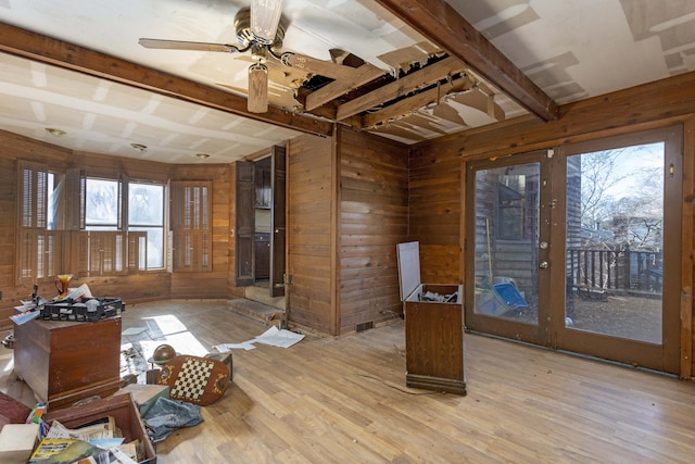 interior space with beam ceiling, wooden walls, ceiling fan, and light wood-type flooring