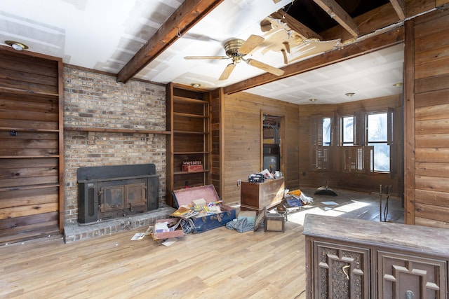 unfurnished living room featuring beam ceiling, light hardwood / wood-style floors, ceiling fan, and wood walls