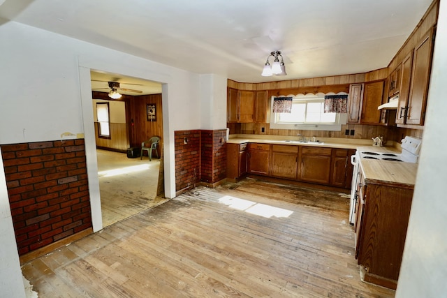 kitchen with sink, electric range, wooden walls, and light hardwood / wood-style floors