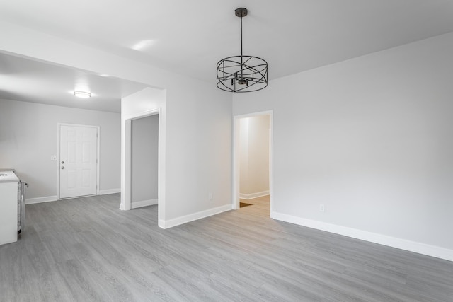 empty room featuring washer / dryer, a chandelier, and light wood-type flooring