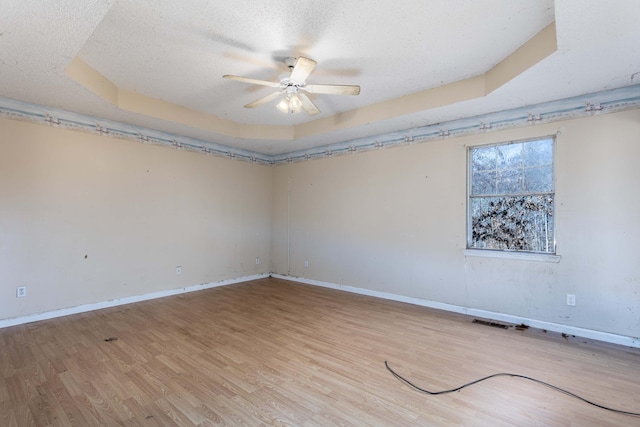 unfurnished room featuring ceiling fan, a tray ceiling, light hardwood / wood-style floors, and a textured ceiling