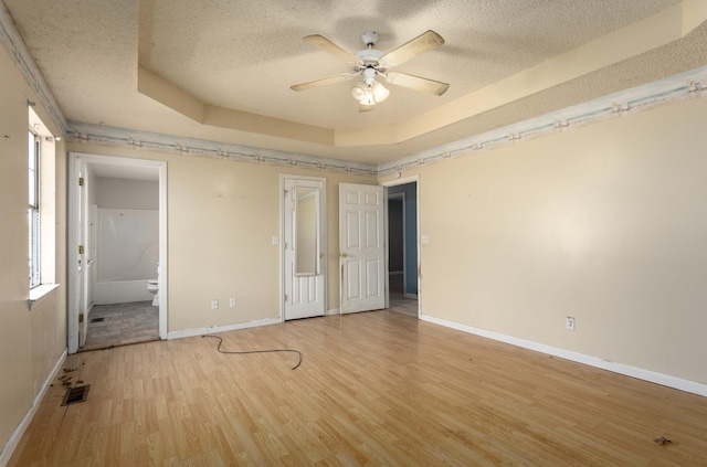 interior space featuring light hardwood / wood-style flooring, a raised ceiling, a textured ceiling, and ensuite bathroom