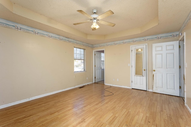 unfurnished bedroom with a tray ceiling, a textured ceiling, and light wood-type flooring