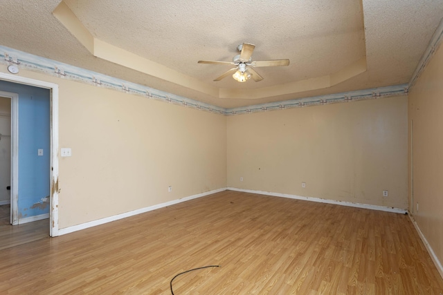 empty room with ceiling fan, a textured ceiling, light hardwood / wood-style floors, and a tray ceiling