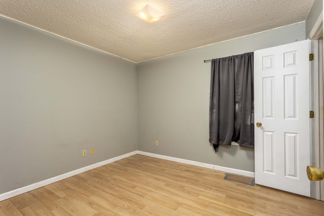 empty room with a textured ceiling and light hardwood / wood-style flooring