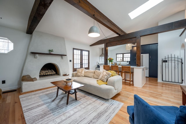 living room featuring a large fireplace, vaulted ceiling with skylight, light hardwood / wood-style floors, and french doors