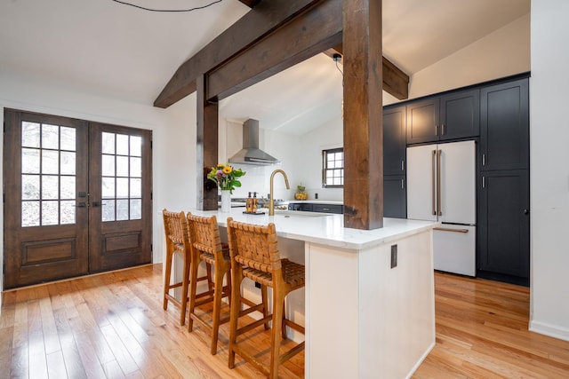 kitchen featuring high end white refrigerator, wall chimney exhaust hood, a breakfast bar, and vaulted ceiling with beams