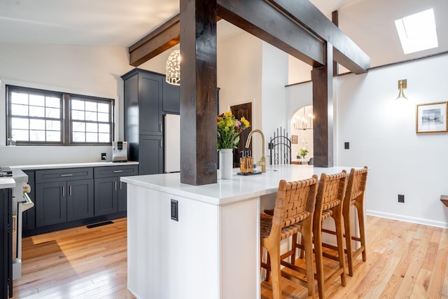 kitchen featuring vaulted ceiling with skylight, refrigerator, a kitchen bar, light hardwood / wood-style floors, and a center island with sink