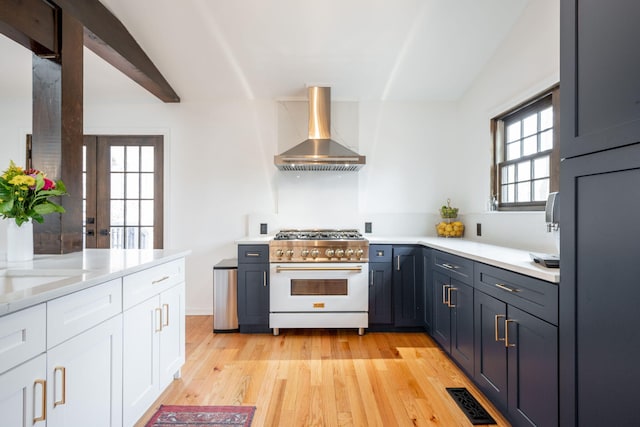 kitchen with beam ceiling, extractor fan, high end stove, white cabinets, and light wood-type flooring