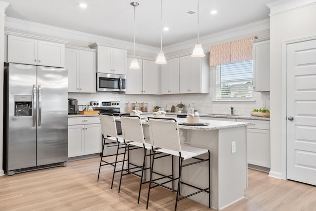 kitchen with a kitchen island with sink, pendant lighting, white cabinets, and appliances with stainless steel finishes