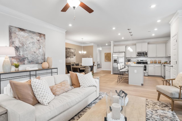 living room with ceiling fan with notable chandelier, ornamental molding, and light wood-type flooring