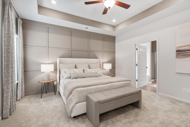 carpeted bedroom with ceiling fan and a tray ceiling