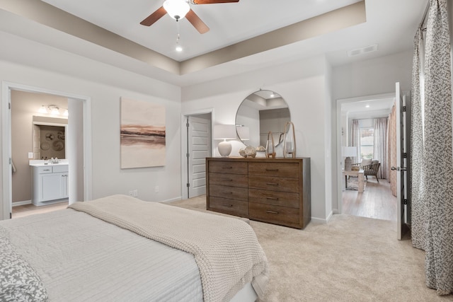 carpeted bedroom featuring sink, a tray ceiling, ceiling fan, and ensuite bathroom