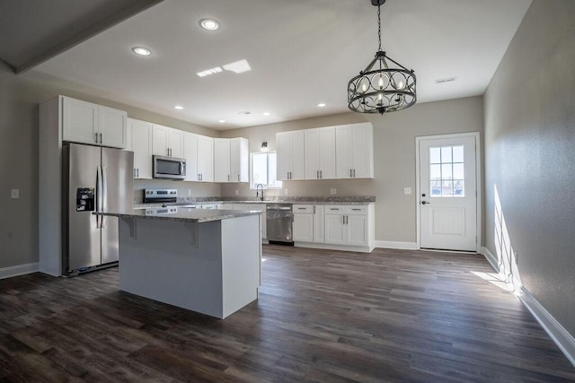 kitchen with white cabinetry, appliances with stainless steel finishes, a kitchen island, stone counters, and pendant lighting