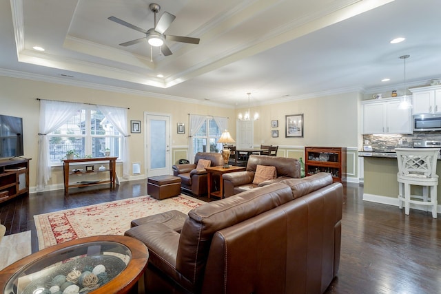 living area with crown molding, a tray ceiling, dark wood finished floors, and ceiling fan with notable chandelier