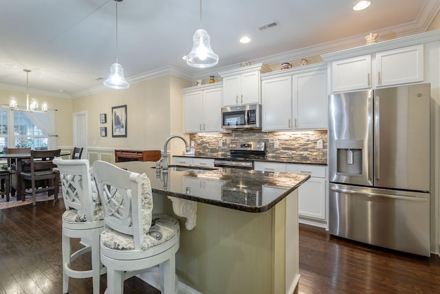 kitchen featuring stainless steel appliances, visible vents, ornamental molding, backsplash, and an island with sink