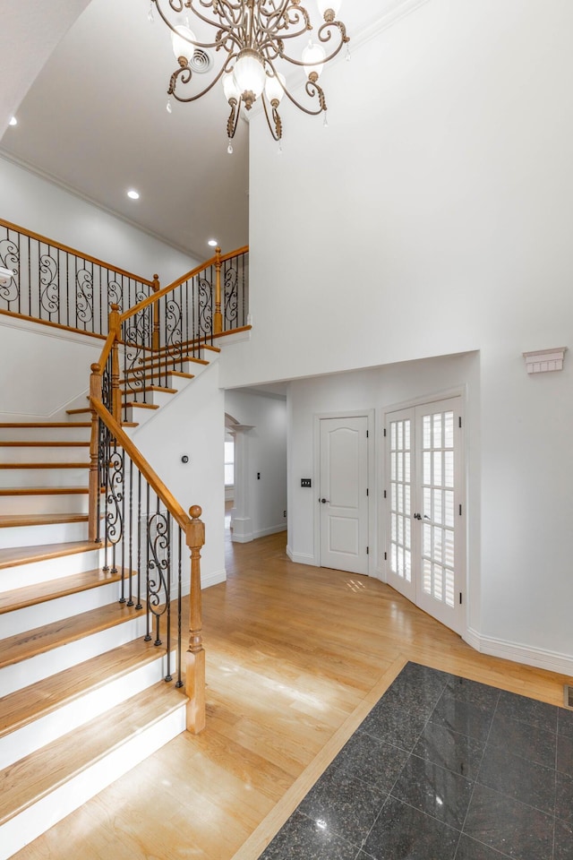 entrance foyer with french doors, a towering ceiling, an inviting chandelier, and hardwood / wood-style floors