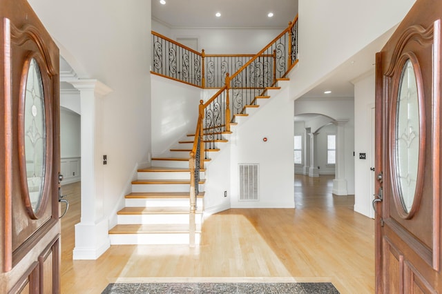 foyer entrance featuring ornamental molding, light hardwood / wood-style floors, decorative columns, and a high ceiling