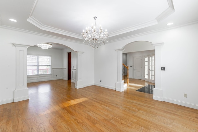 spare room with a notable chandelier, a tray ceiling, light wood-type flooring, and ornate columns