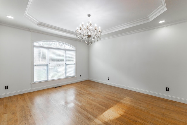 empty room featuring a raised ceiling, crown molding, a chandelier, and light wood-type flooring