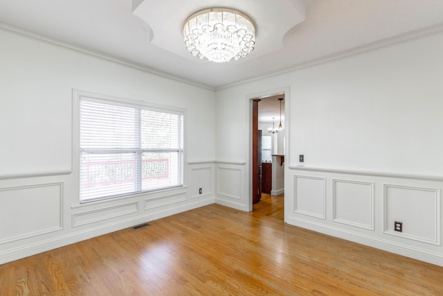 empty room with crown molding, a chandelier, and light hardwood / wood-style flooring