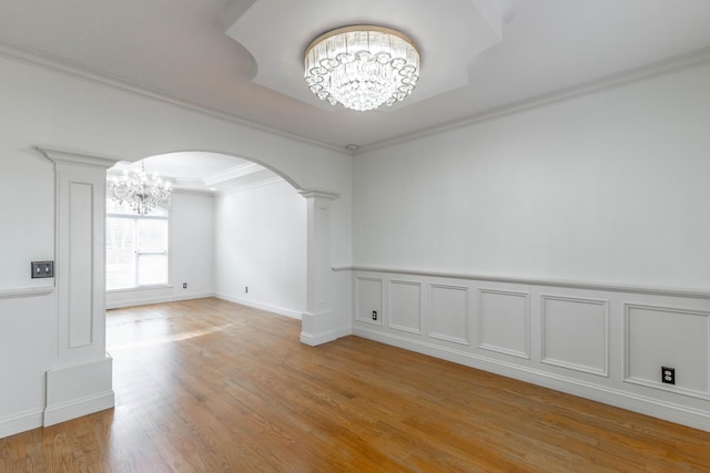 empty room with ornate columns, crown molding, a chandelier, and light hardwood / wood-style floors