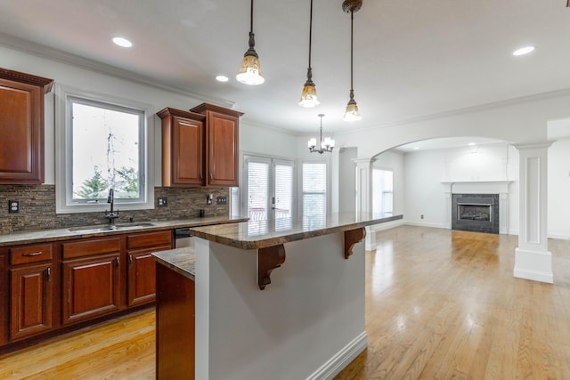 kitchen featuring a kitchen bar, sink, a center island, hanging light fixtures, and decorative columns