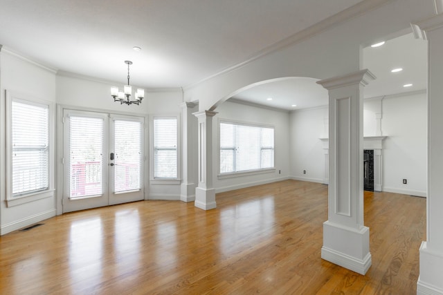 unfurnished living room featuring french doors, crown molding, a chandelier, light hardwood / wood-style flooring, and decorative columns