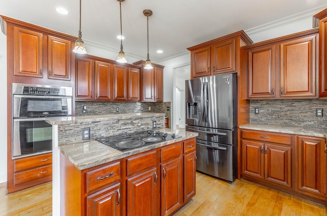 kitchen with hanging light fixtures, appliances with stainless steel finishes, light stone counters, and light hardwood / wood-style flooring