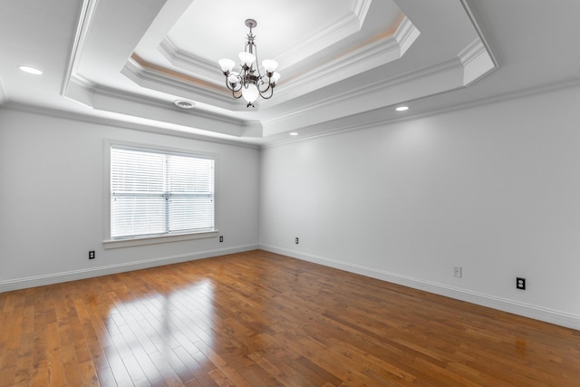 empty room with hardwood / wood-style flooring, a tray ceiling, a chandelier, and crown molding