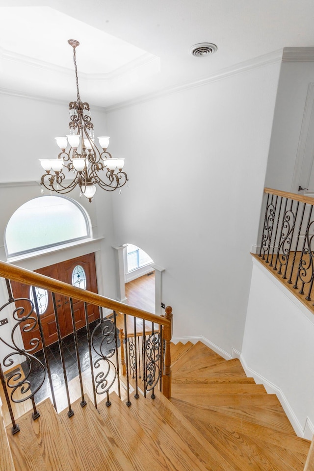 staircase featuring a towering ceiling, ornamental molding, hardwood / wood-style floors, and a notable chandelier