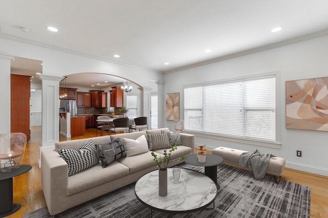 living room featuring a notable chandelier, ornamental molding, decorative columns, and light hardwood / wood-style floors