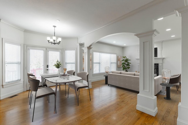 dining area featuring crown molding, a notable chandelier, light hardwood / wood-style floors, and ornate columns