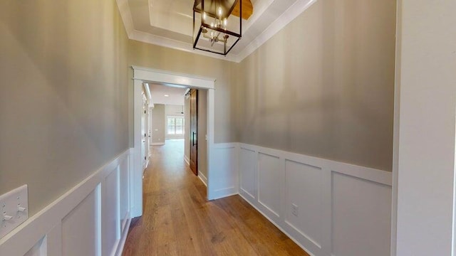 hall with crown molding, a raised ceiling, light hardwood / wood-style floors, and a notable chandelier
