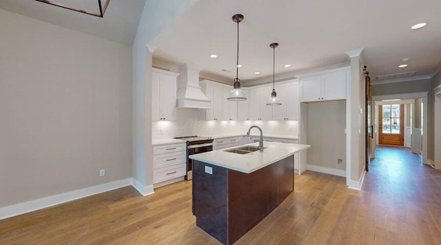 kitchen with sink, stainless steel range with electric stovetop, white cabinetry, an island with sink, and custom exhaust hood