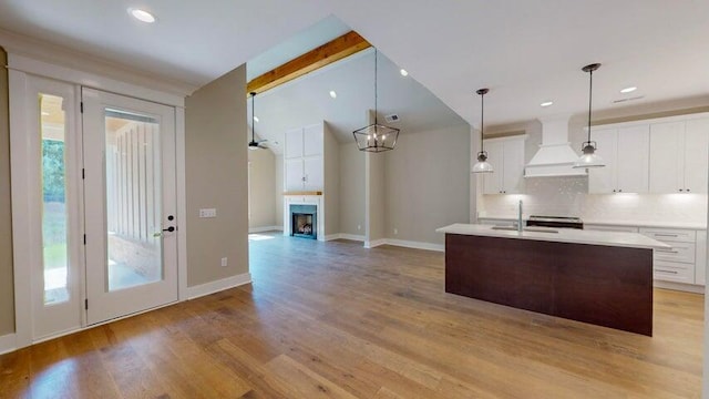 kitchen featuring premium range hood, sink, white cabinetry, an island with sink, and pendant lighting