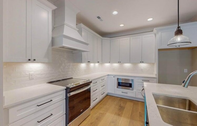 kitchen featuring sink, custom exhaust hood, white cabinetry, hanging light fixtures, and electric stove