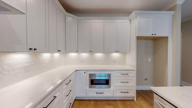 kitchen featuring white cabinetry, light stone countertops, light hardwood / wood-style floors, and backsplash