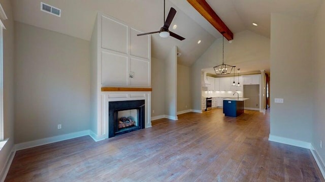 unfurnished living room with high vaulted ceiling, hardwood / wood-style flooring, beamed ceiling, a fireplace, and ceiling fan with notable chandelier