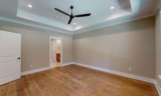 unfurnished bedroom with ensuite bath, a raised ceiling, and light wood-type flooring