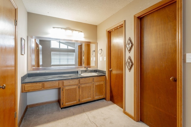 bathroom with a textured ceiling, carpet floors, vanity, and baseboards